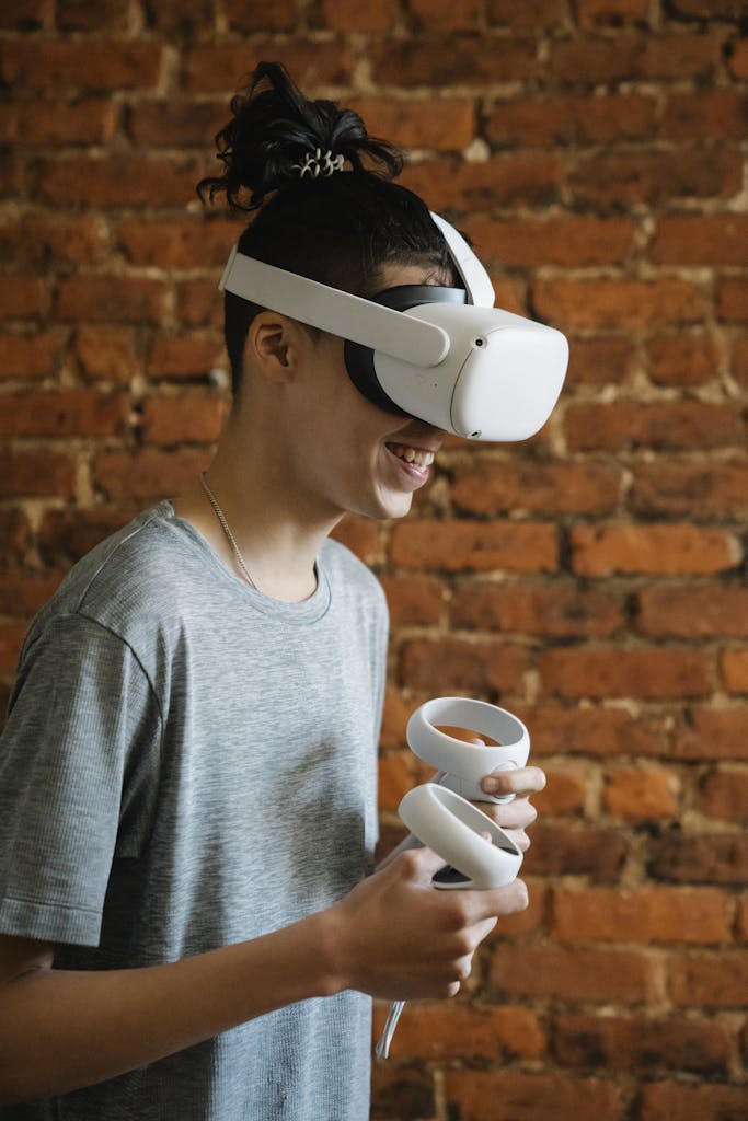 Side view of male teen in modern glasses smiling while experiencing virtual reality and playing videogame